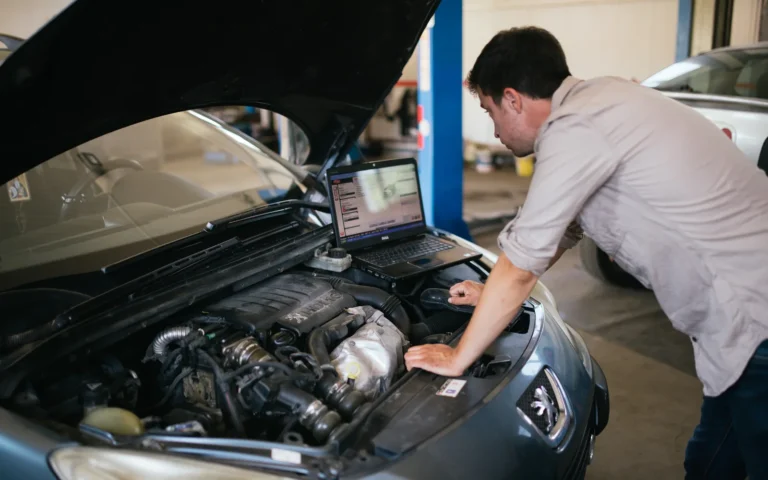 A technician uses a laptop-based diagnostic tool at the front of a car in a workshop